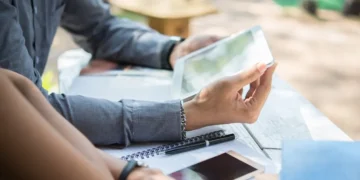 Duas pessoas utilizando dispositivos móveis e um tablet, representando a consulta ao informe de rendimentos do PicPay para a declaração do IR 2025.