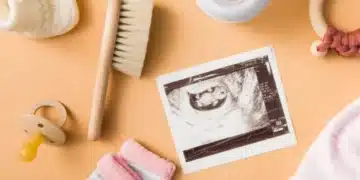 Itens essenciais para o enxoval de bebê, incluindo sapatinho, chupeta, mamadeira, escova, mordedor, touca e uma foto de ultrassom.