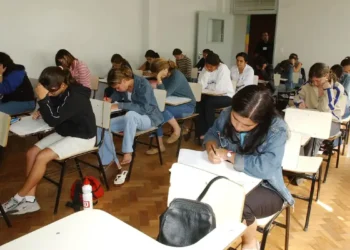 Alunos do ensino médio realizado prova em sala de aula, representando os critérios para participação no programa Pé-de-Meia 2025.