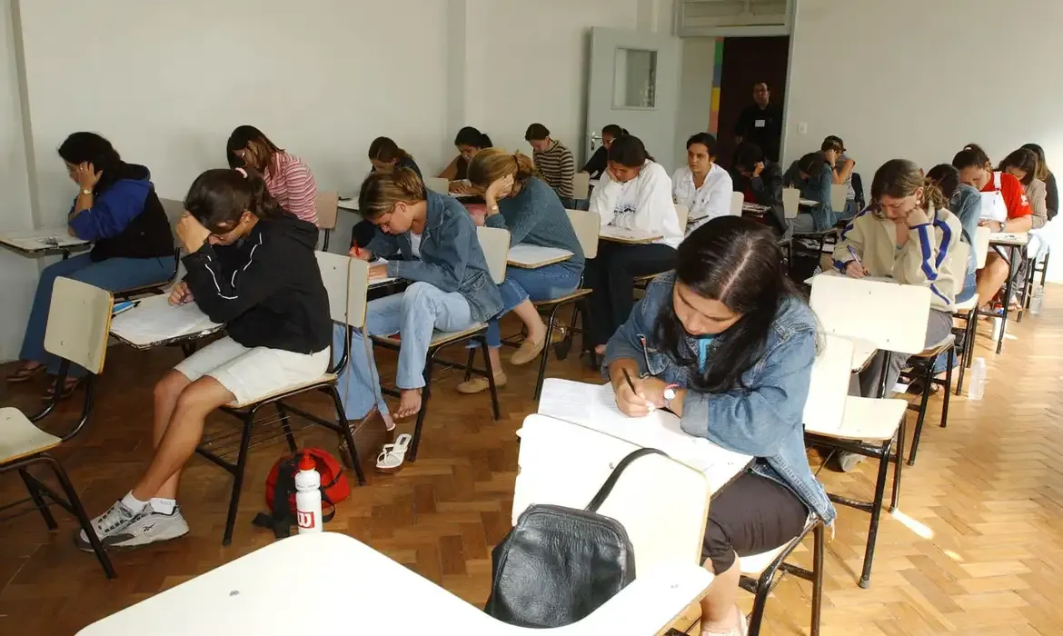 Alunos do ensino médio realizado prova em sala de aula, representando os critérios para participação no programa Pé-de-Meia 2025.