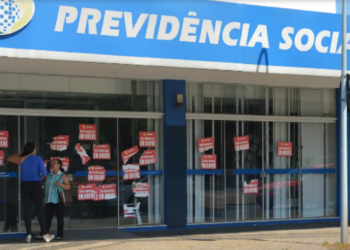 Fachada de uma agência do INSS com cartazes de greve nos vidros.