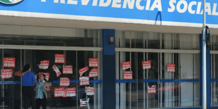 Fachada de uma agência do INSS com cartazes de greve nos vidros.