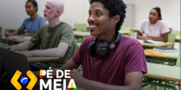 Estudantes em sala de aula, com foco em um jovem sorridente no primeiro plano, enquanto outros estão em segundo plano. Imagem relacionada ao calendário de pagamentos antecipados do programa Pé-de-meia para 2025.