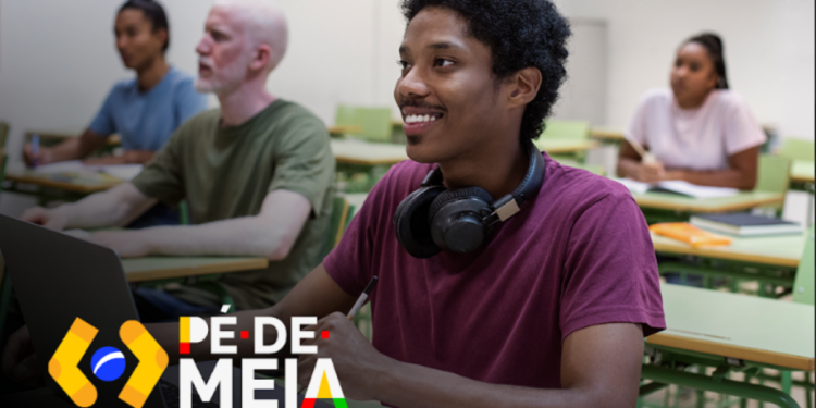 Estudantes em sala de aula, com foco em um jovem sorridente no primeiro plano, enquanto outros estão em segundo plano. Imagem relacionada ao calendário de pagamentos antecipados do programa Pé-de-meia para 2025.
