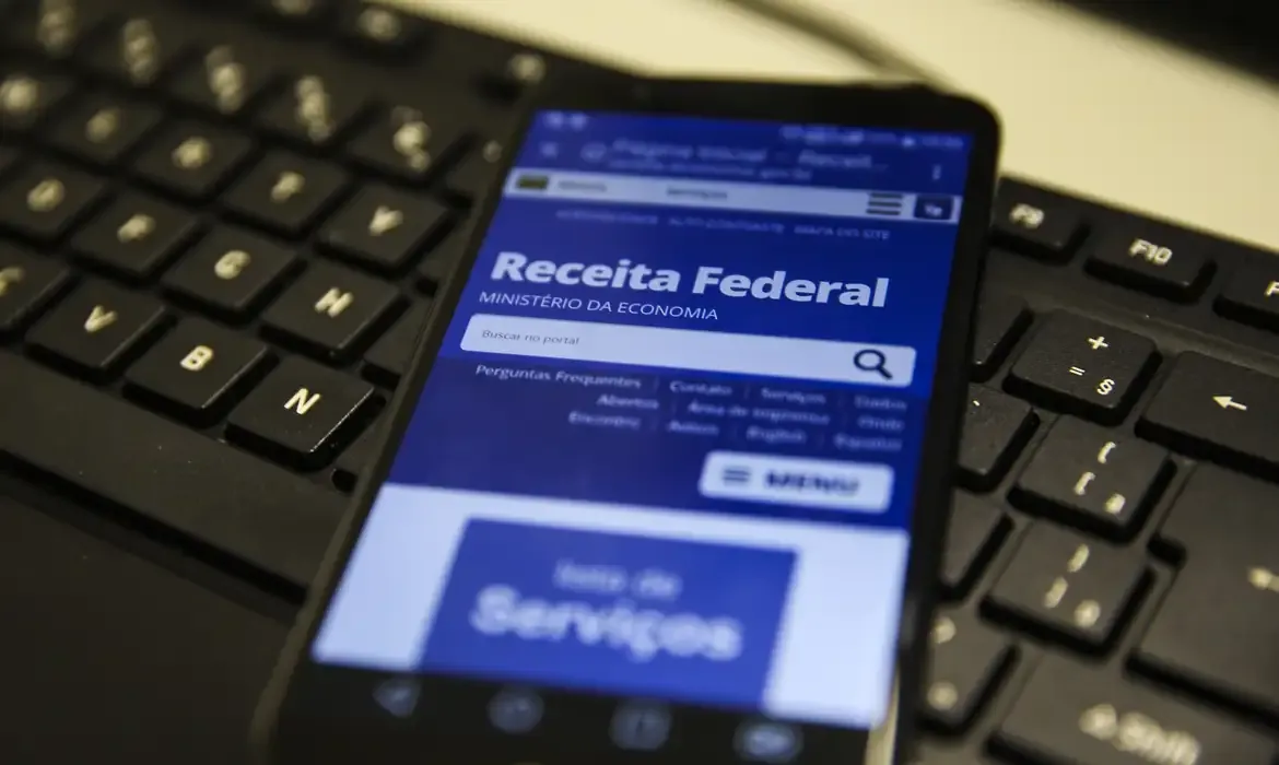 Celular com o site da Receita Federal aberto, suportado em um teclado de computador.