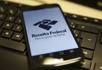 "Logo da Receita Federal no celular, com foco no aplicativo Meu Imposto de Renda, em fundo de teclado de computador."