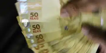 Mão segurando cédulas de 50 reais em movimento, representando saque de dinheiro.
