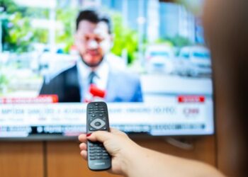 Homem assistindo à TV com controle remoto, transmitindo conteúdo de entretenimento
