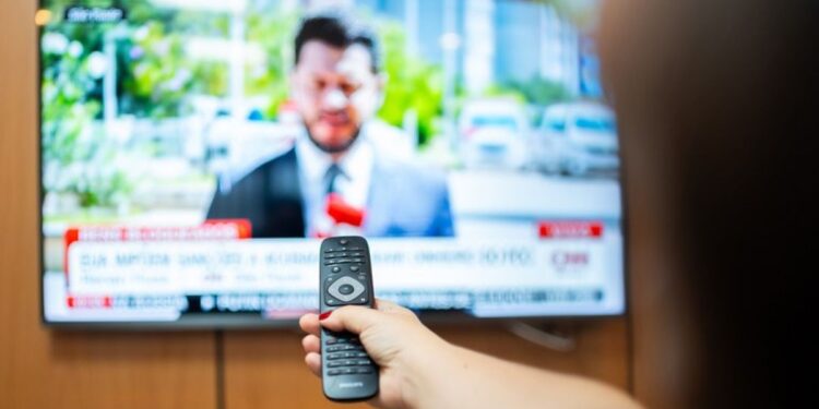 Homem assistindo à TV com controle remoto, transmitindo conteúdo de entretenimento