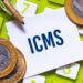 Imagem de moedas e calculadora com a palavra ICMS destacada.