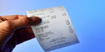 Pessoa segurando nota fiscal detalhada contra fundo azul
