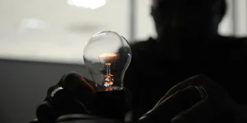 Pessoa segurando lâmpada acesa com pouca iluminação ao redor
