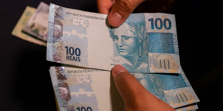 Pessoa contando notas de 100 reais com foco na nota