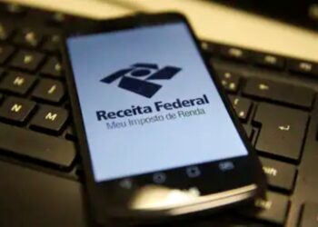 Logo da Receita Federal exibido em um smartphone com teclado ao fundo.