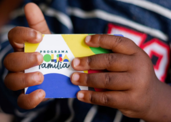 Cartão do programa Bolsa Família sendo segurado por uma criança, simbolizando a liberação do pagamento antecipado para 659 municípios.