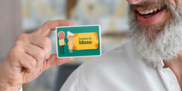 Homem sorridente segurando uma representação ilustrada da Carteira do Idoso nas mãos.