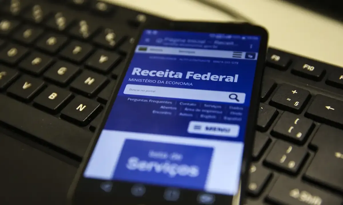 Tela do site da Receita Federal exibida em um celular sobre teclado de computador.