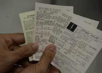 Mão segurando vários cupons fiscais com CPF informado nas compras.