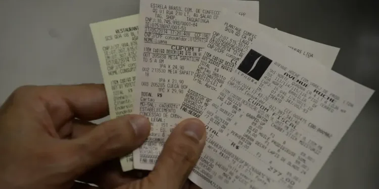 Mão segurando vários cupons fiscais com CPF informado nas compras.