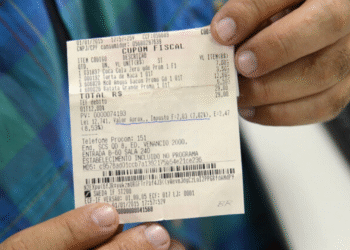 Pessoa segurando um cupom fiscal com CPF, ilustrando participação em sorteio de prêmios ao incluir CPF na nota.