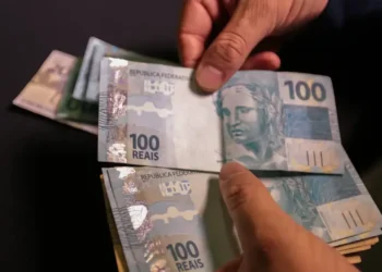 Cédulas de 100 reais sendo contadas, representando a importância do Devolve ICMS 2025.