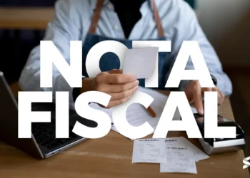 Pessoa segurando nota fiscal ao lado de um notebook e máquina de cartão, com destaque para o texto “Nota Fiscal”