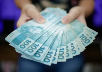 Mãos segurando cédulas de R$100 representando a premiação do programa Nota da Gente