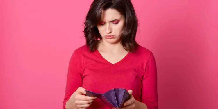 Mulher jovem olhando carteira vazia com expressão de preocupação.