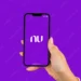 Mão segurando um smartphone exibindo o logotipo do Nubank com um fundo roxo.