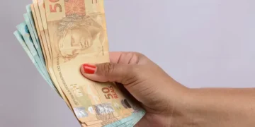Mão segurando cédulas de reais representando o pagamento do Cartão Escola 10