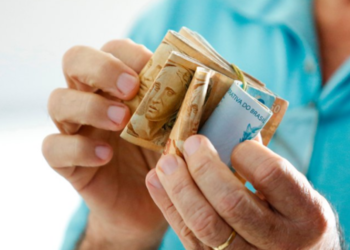 Pessoa segurando cédulas de dinheiro brasileiro, simbolizando o reajuste do salário mínimo em 2025.