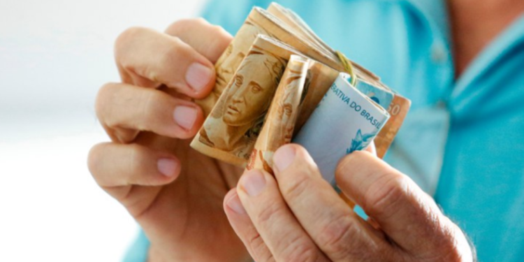 Pessoa segurando cédulas de dinheiro brasileiro, simbolizando o reajuste do salário mínimo em 2025.
