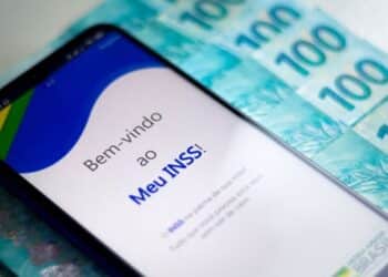 Imagem do aplicativo Meu INSS exibido em um celular, com cédulas de 100 reais ao fundo, representando a facilidade de acesso aos serviços do INSS.