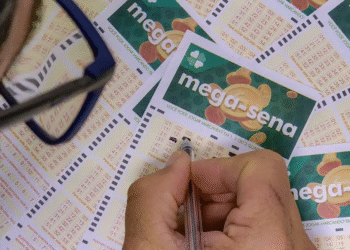Imagem de um apostador preenchendo seu bilhete da Mega-Sena, com vários cupons em cima da mesa, representando a chance de ganhar o prêmio acumulado deste sábado.