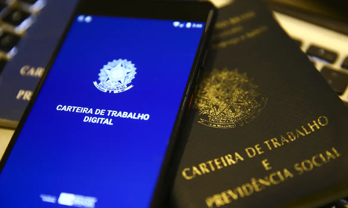 Aplicativo da Carteira de Trabalho Digital aberto em um smartphone ao lado da carteira física.