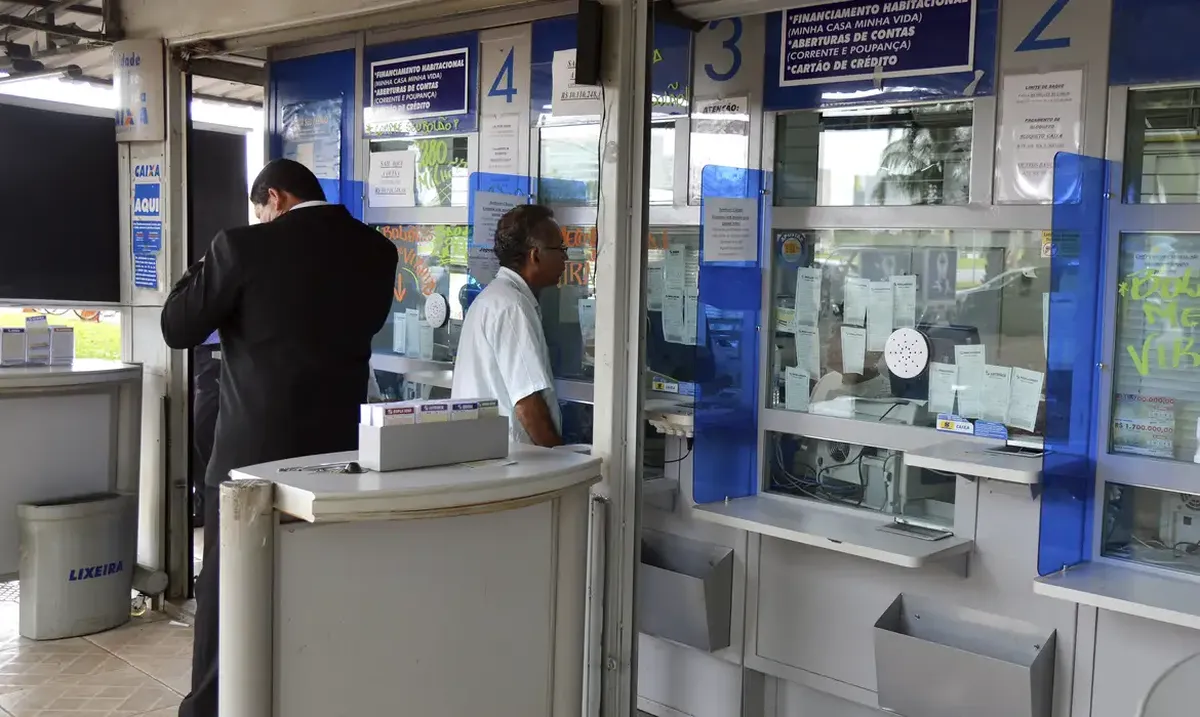 Caixa de atendimento com pessoas aguardando e sendo atendidas em lotérica para apostas da Mega-Sena.