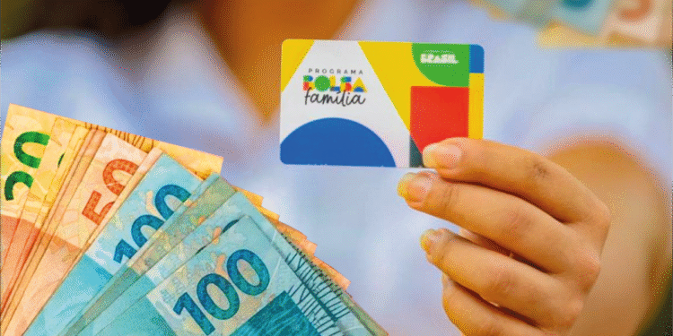Pessoa segurando cartão do Programa Bolsa Família com cédulas de dinheiro ao lado.