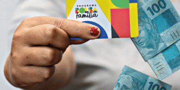 Cartão do Bolsa Família e cédulas de R$ 100, representando o impacto financeiro da mudança no benefício extraordinário.