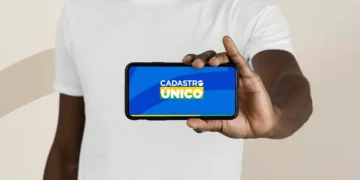 Pessoa segurando celular com a tela exibindo logo do Cadastro Único em fundo azul