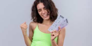 Mulher jovem sorridente segurando bilhetes da Nota Premiada Bahia, com fundo neutro./ Imagem: Freepik