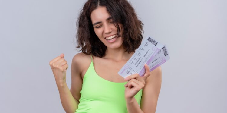 Mulher jovem sorridente segurando bilhetes da Nota Premiada Bahia, com fundo neutro./ Imagem: Freepik