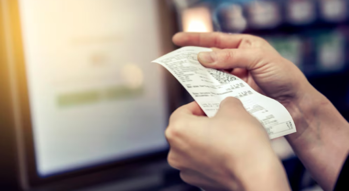 Pessoa segurando e conferindo um cupom fiscal em ambiente de compras.