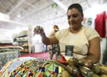 "Mulher bordando peças com cores vibrantes, representando o trabalho artesanal no programa Acredita no Primeiro Passo."