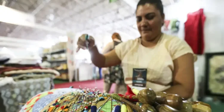 "Mulher bordando peças com cores vibrantes, representando o trabalho artesanal no programa Acredita no Primeiro Passo."