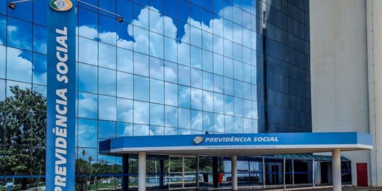 Fachada do prédio da Previdência Social com reflexo do céu azul nas janelas de vidro.
