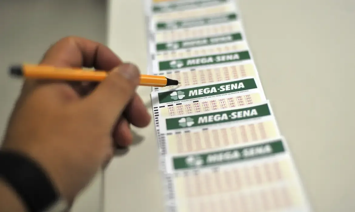 Pessoa segurando caneta enquanto preenche volante de apostas da Mega-Sena.