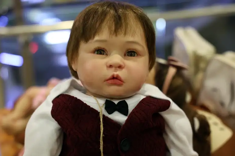 Bebê reborn com roupa formal e laço preto, com expressão realista e detalhes delicados.
