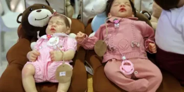 Bonecas bebê reborn realistas de tamanho grande com roupas cor-de-rosa, descansando sobre almofadas em formato de urso.