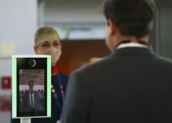 Pessoa passando por um sistema de biometria facial em um ambiente público, com um dispositivo de reconhecimento facial em operação.