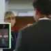 Pessoa passando por um sistema de biometria facial em um ambiente público, com um dispositivo de reconhecimento facial em operação.